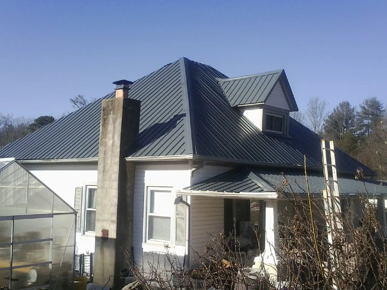 Dark blue standing seam metal roof on a white farmhouse with dormer — Slate & Tile Roof Repair by Roofing Brothers in Guthrie Center