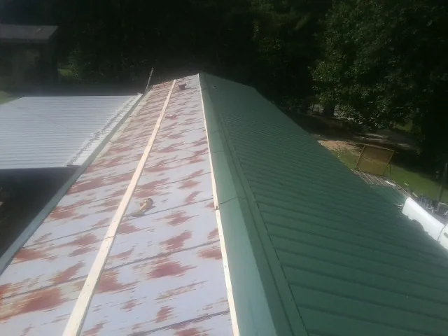Old rusted panels beside newly installed green metal roofing — Wind Damage Roof Repair by Roofing Brothers in Guthrie Center