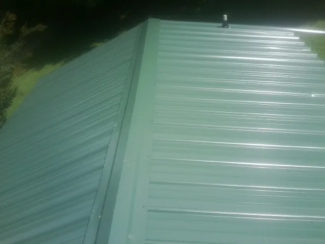 New green metal panels meeting at the ridge of a roof — Flat Roof Repair work by our crew in Guthrie Center