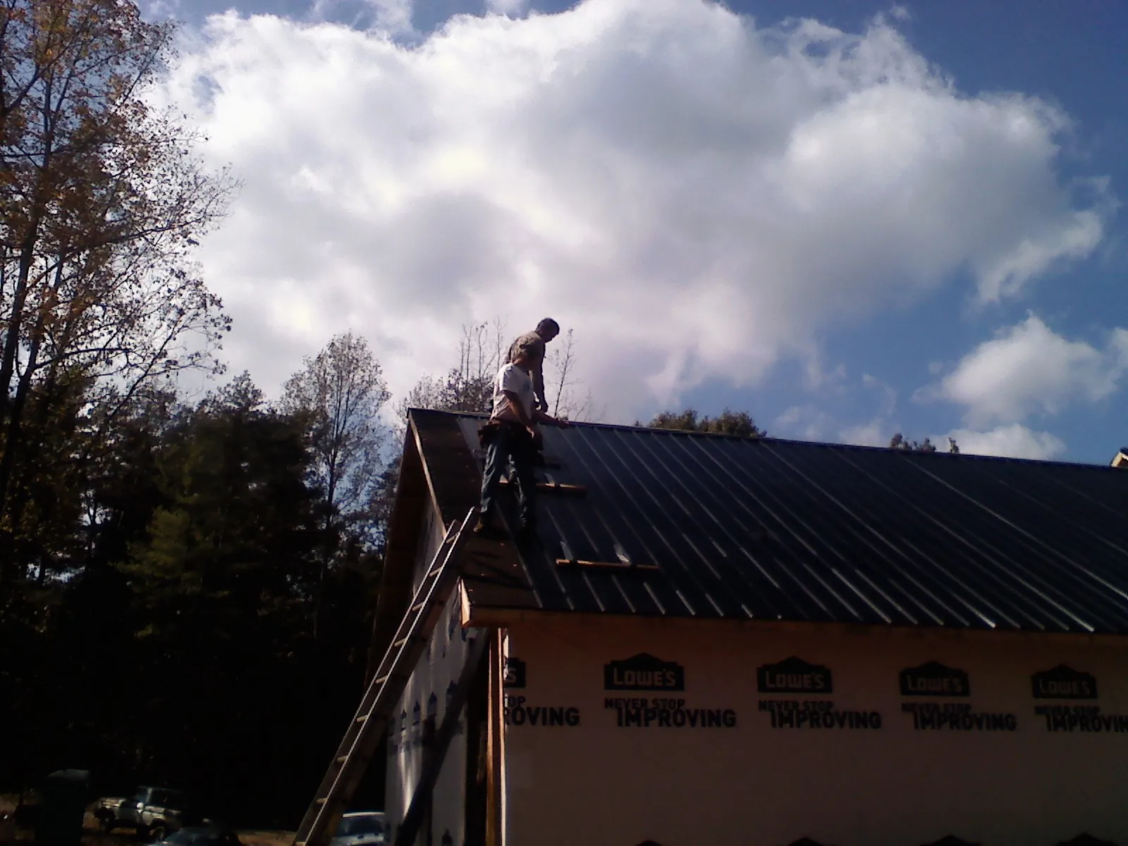 Roofer fastening dark metal panels high against a cloudy sky, from a Roof Inspection job in Guthrie Center