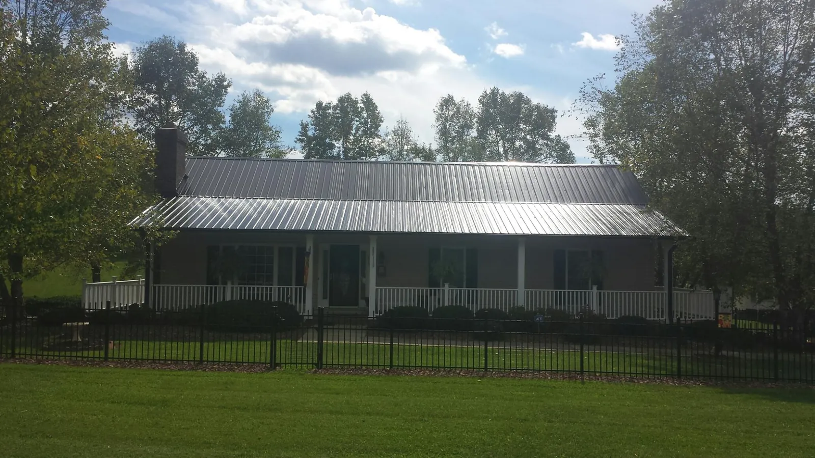 Gray metal roof on a brick ranch with a full width front porch — Gutter Guard Installation work by our crew in Guthrie Center