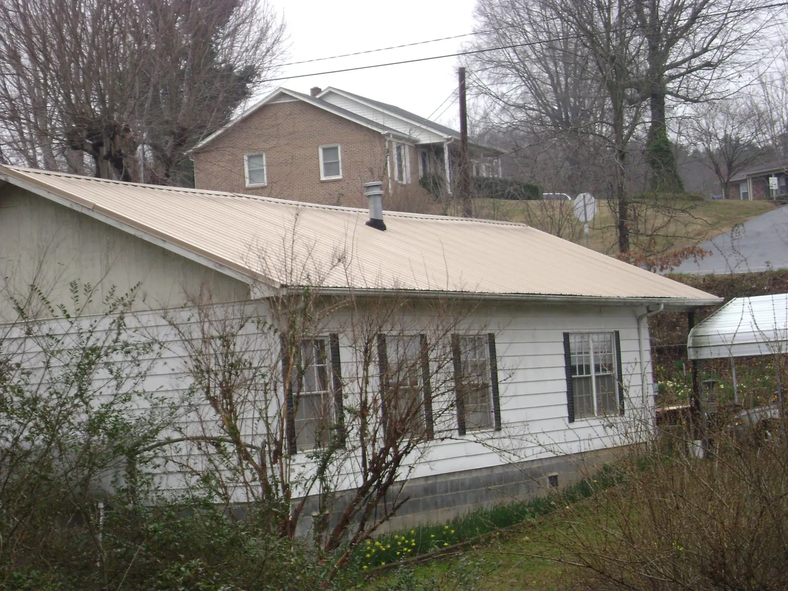 Tan metal roof on a white sided house set into a hillside — Commercial Roofing by Roofing Brothers in Guthrie Center