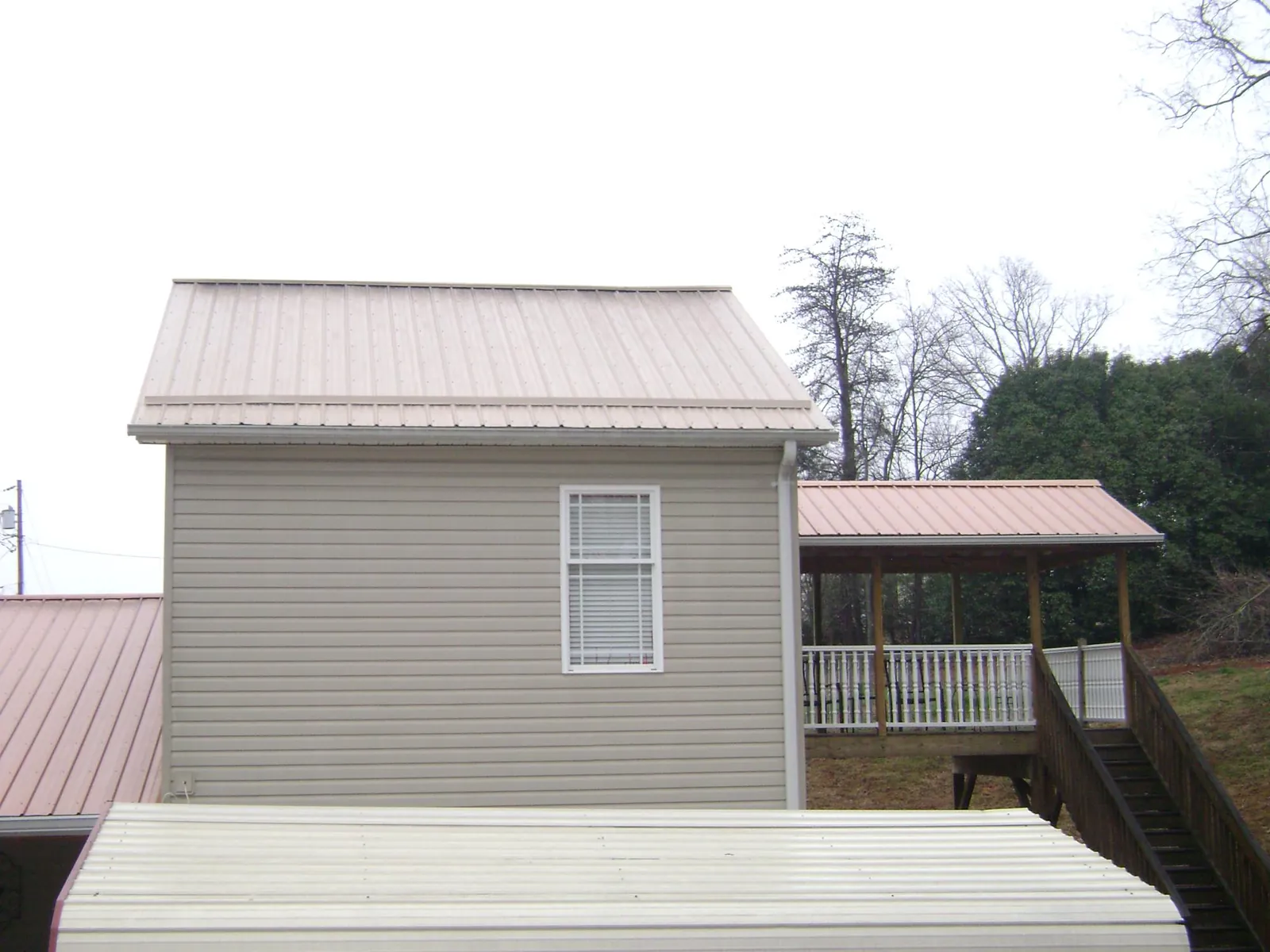 Tan metal roofs on a two story addition and attached porch, from a Roof Replacement job in Guthrie Center